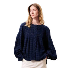 Load image into Gallery viewer, A woman stands against a plain light beige wall wearing a dark navy blue plaid long-sleeve top, cream wide-leg trousers, and dark navy shoes.
