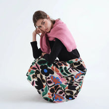 Load image into Gallery viewer, A model wearing a vibrant floral print skirt with a pink knit sweater draped over her shoulders and a black long-sleeve top, posing against a plain white studio background.