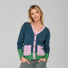 Load image into Gallery viewer, A woman modeling a teal and pink color-blocked cardigan with green cuffs, paired with patterned wide-leg pants, pink socks, and green sneakers, against a light gray studio background.
