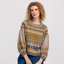 Load image into Gallery viewer, A woman with curly blonde hair wearing a patterned knit sweater and blue jeans, standing against a light gray studio background.
