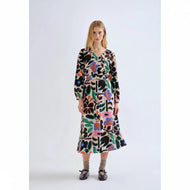 A woman stands against a plain light gray studio background wearing a long-sleeve midi dress with an abstract multicolor print. The dress has a black base with large organic shapes in pink, green, orange, blue, and cream.