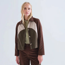 Load image into Gallery viewer, A blonde model stands against a light gray studio background wearing a brown and beige color-block corduroy jacket over a green striped shirt, paired with brown corduroy trousers.
