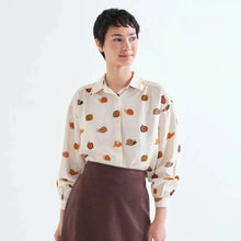 Load image into Gallery viewer, A model wearing a cream-colored long-sleeve blouse with a pumpkin print, tucked into a dark brown ruffled mini skirt, paired with mustard yellow tights, against a plain white studio background.
